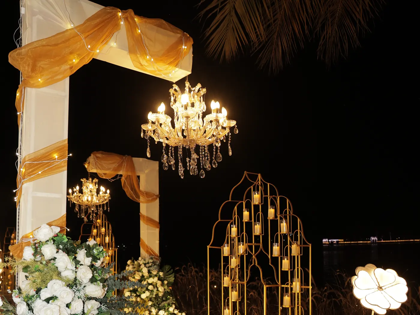 A chandelier, gold drapes and white flowers set up for a celebration at Nehamrit Farms